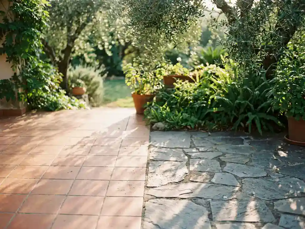 Keramische tegels en natuurstenen bestrating op een tuinterras, met terracotta en leisteengrijze tinten in middagzonlicht.