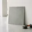 Grote 60x60 cm keramische tegel met matte betonlook in grijs, leunend tegen witte showroomwand met tegelzuignappen op de vloer.