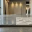 Twee keramische tegels op showroomvloer: één gladgeglazuurd, één met reliëf, met waterdruppels en zachte zijdelingse belichting.