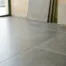 Grote keramische vloertegels in betongrijs mat met strakke voegen en gestapelde tegels op de achtergrond in een tegelshowroom.